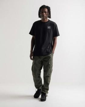 A man with dreads wearing a black Herschel logo t-shirt and green cargo pants