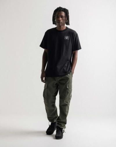 A man with dreads wearing a black Herschel logo t-shirt and green cargo pants