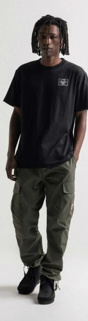 A man with dreads wearing a black Herschel logo t-shirt and green cargo pants