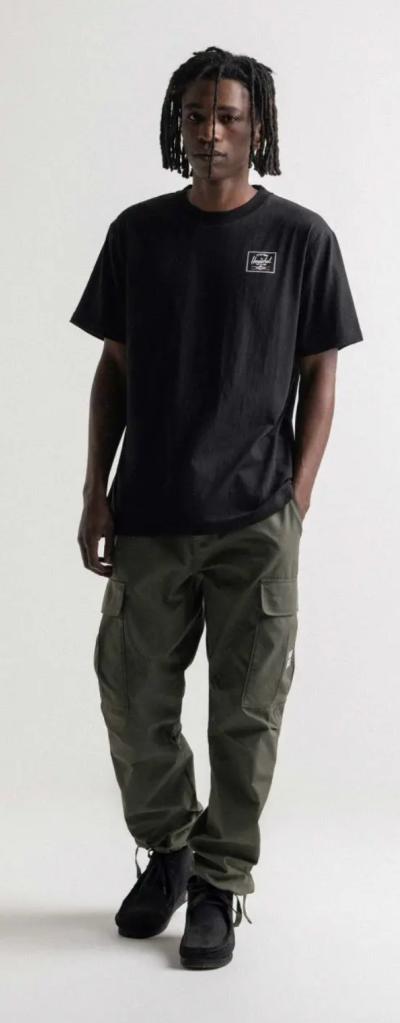 A man with dreads wearing a black Herschel logo t-shirt and green cargo pants