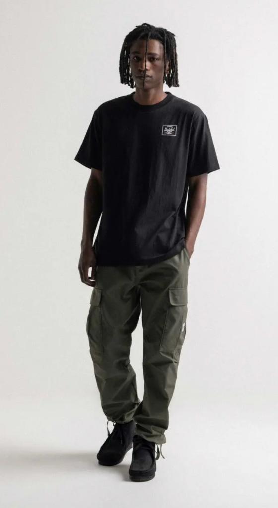 A man with dreads wearing a black Herschel logo t-shirt and green cargo pants