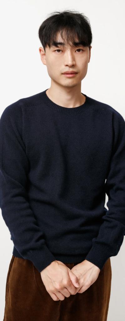 A man wearing a navy blue Neighbour sweatshirt and brown pants on a white backdrop