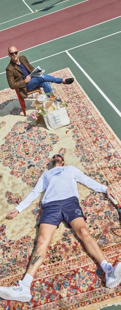 A man wearing a white Palmes Tennis long-sleeve while laying on a persian rug atop of tennis court