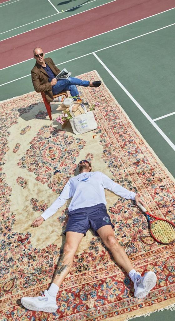 A man wearing a white Palmes Tennis long-sleeve while laying on a persian rug atop of tennis court