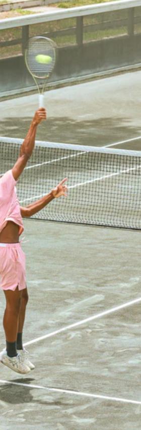 A man serving on a tennis court while wearing a pink Sigrun tennis outfit