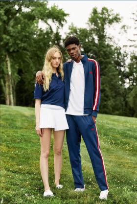 A couple wearing navy blue boast tennis outfits standing on a grassy knoll