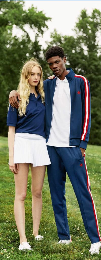 A couple wearing navy blue boast tennis outfits standing on a grassy knoll