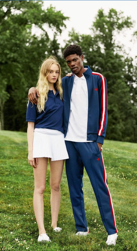 A couple wearing navy blue boast tennis outfits standing on a grassy knoll