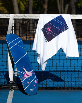 A white t-shirt with a tennis court print on it draped over a tennis court net with a matching skateboard balanced beside it