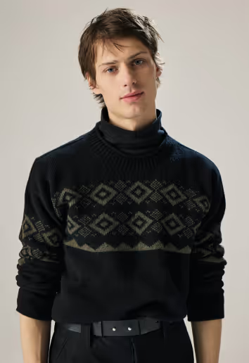 A man wearing a navy blue turtleneck sweatshirt with the sleeves rolled up