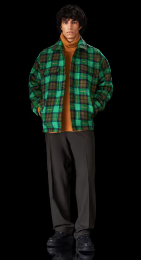 A man wearing a brown Samsoe Samsoe turtleneck underneath a green checkered jacket and black pants