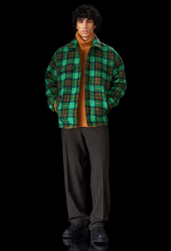 A man wearing a brown Samsoe Samsoe turtleneck underneath a green checkered jacket and black pants