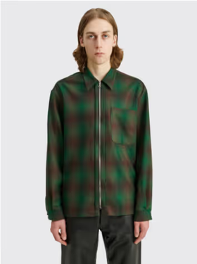 A man with long hair wearing a Tres-Bien checkered green and black zip jacket and brown pants