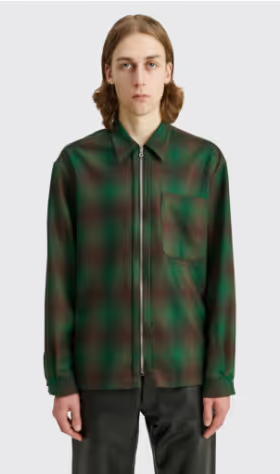 A man with long hair wearing a Tres-Bien checkered green and black zip jacket and brown pants