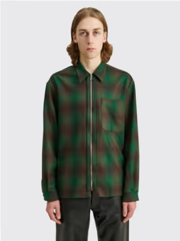 A man with long hair wearing a Tres-Bien checkered green and black zip jacket and brown pants