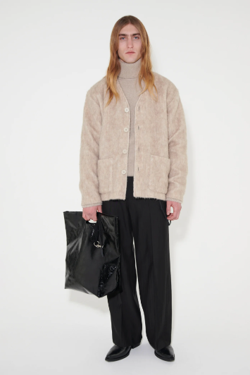 A man in a brown fluffy Our Legacy cardigan with a matching brown turtleneck and black pants holding a black bag