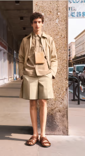 A man wearing a brown A.P.C. outfit which includes shorts, a short-sleeve button up under a long-sleeve button up and a bag
