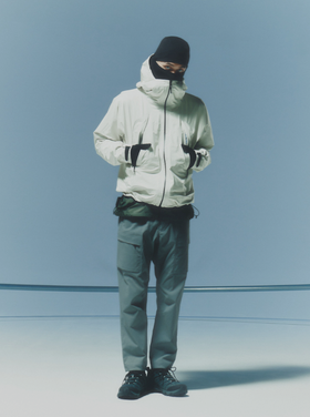 A man waring a white Goldwin jacket, grey pants and a black beanie along with black shoes and gloves