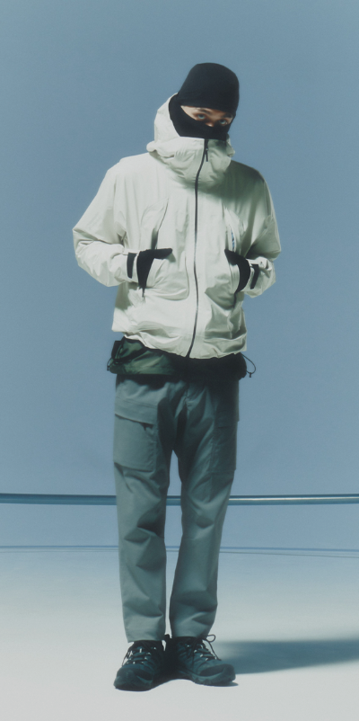 A man waring a white Goldwin jacket, grey pants and a black beanie along with black shoes and gloves