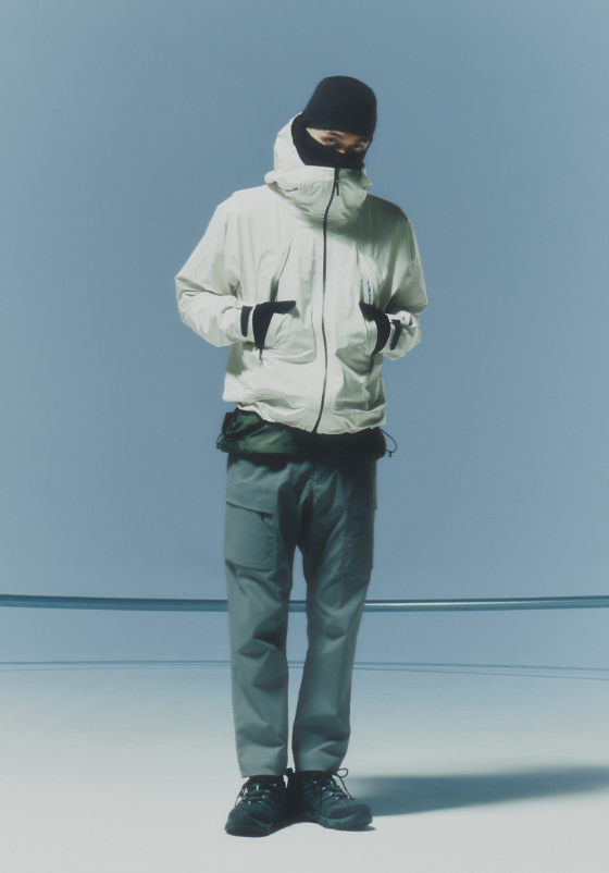 A man waring a white Goldwin jacket, grey pants and a black beanie along with black shoes and gloves