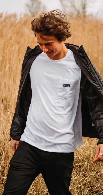 A man in a wheat field wearing a white Patagonia t-shirt along with black jacket and pants