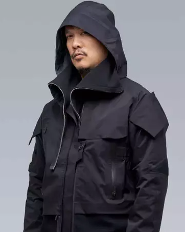 A man wearing a black Acronym jacket with his hood on