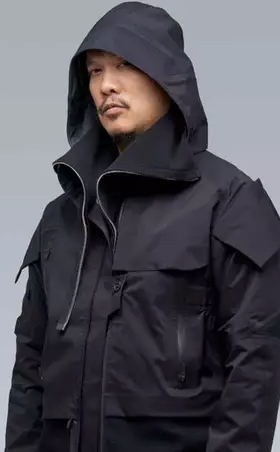 A man wearing a black Acronym jacket with his hood on