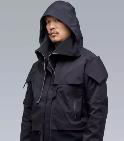 A man wearing a black Acronym jacket with his hood on