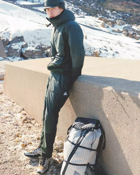 A man wearing a green And Wander snow suit with a matching green hat and salomon shoes