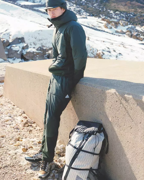 A man wearing a green And Wander snow suit with a matching green hat and salomon shoes