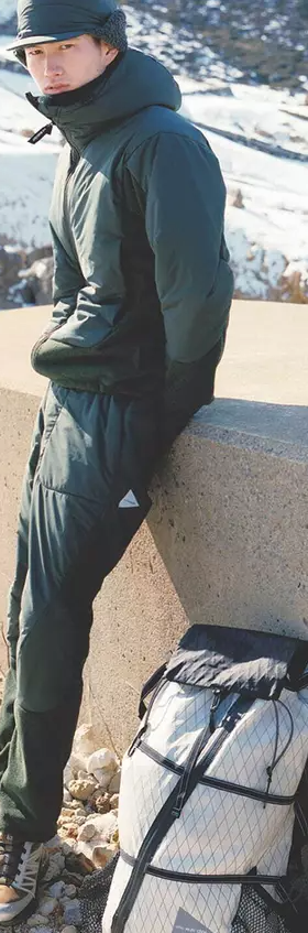 A man wearing a green And Wander snow suit with a matching green hat and salomon shoes