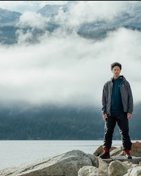 A man standing on rocks just off a lake wearing a Arc-teryx jacket, hoodie and pants