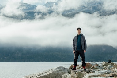 A man standing on rocks just off a lake wearing a Arc-teryx jacket, hoodie and pants