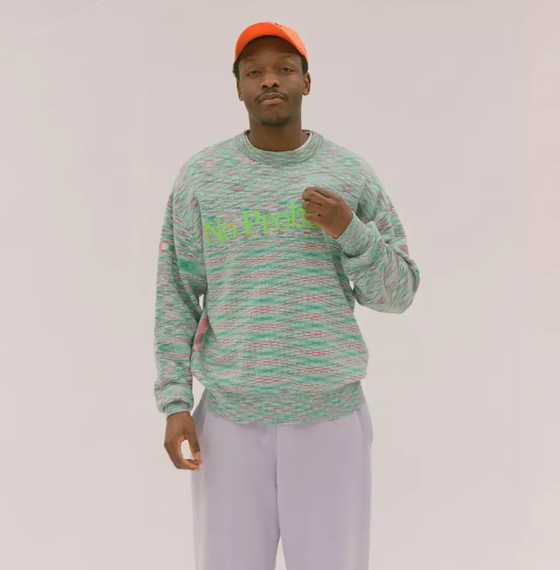 A man in a colorful Aries green sweater, lavender pants and an orange hat