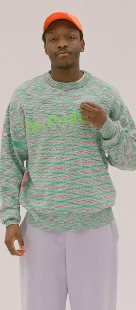 A man in a colorful Aries green sweater, lavender pants and an orange hat