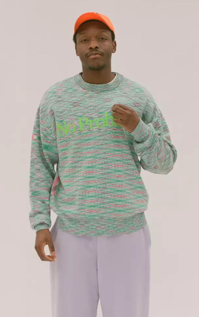 A man in a colorful Aries green sweater, lavender pants and an orange hat