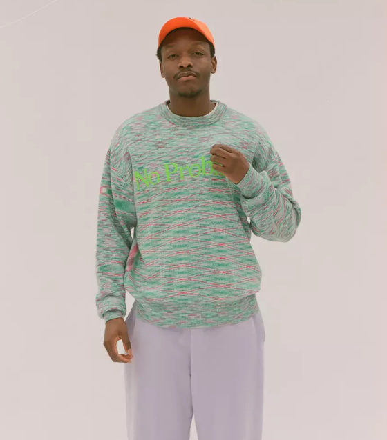 A man in a colorful Aries green sweater, lavender pants and an orange hat