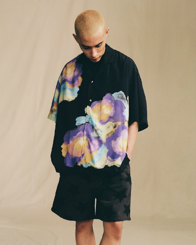 A man in a black Awake NY short-sleeve button up with a colorful floral print and black shorts