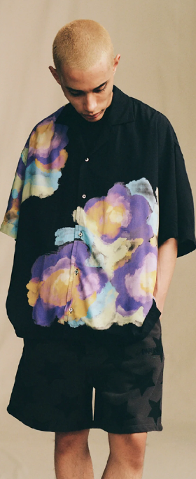 A man in a black Awake NY short-sleeve button up with a colorful floral print and black shorts