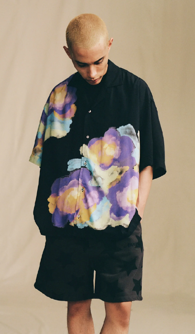 A man in a black Awake NY short-sleeve button up with a colorful floral print and black shorts