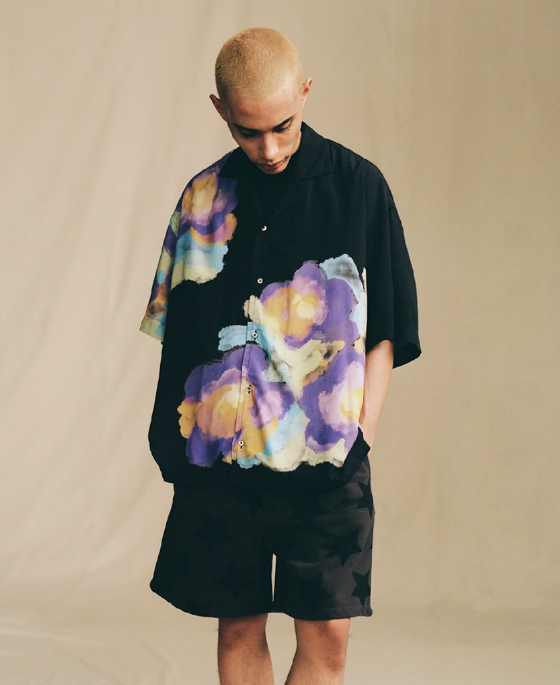 A man in a black Awake NY short-sleeve button up with a colorful floral print and black shorts