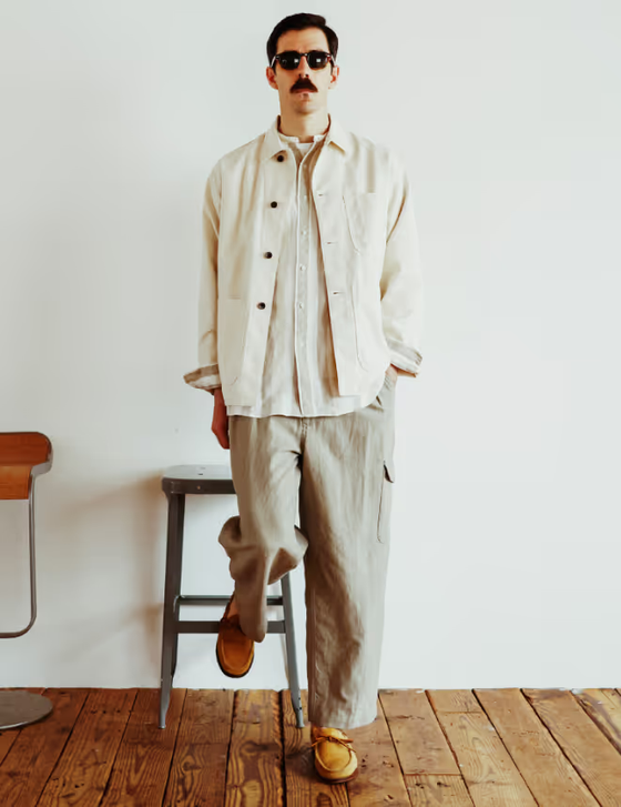 A man in sunglasses wearing a Beams Plus beige overshirt with oversized grey pants and brown shoes