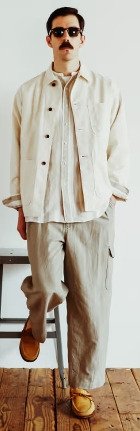 A man in sunglasses wearing a Beams Plus beige overshirt with oversized grey pants and brown shoes
