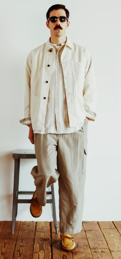 A man in sunglasses wearing a Beams Plus beige overshirt with oversized grey pants and brown shoes
