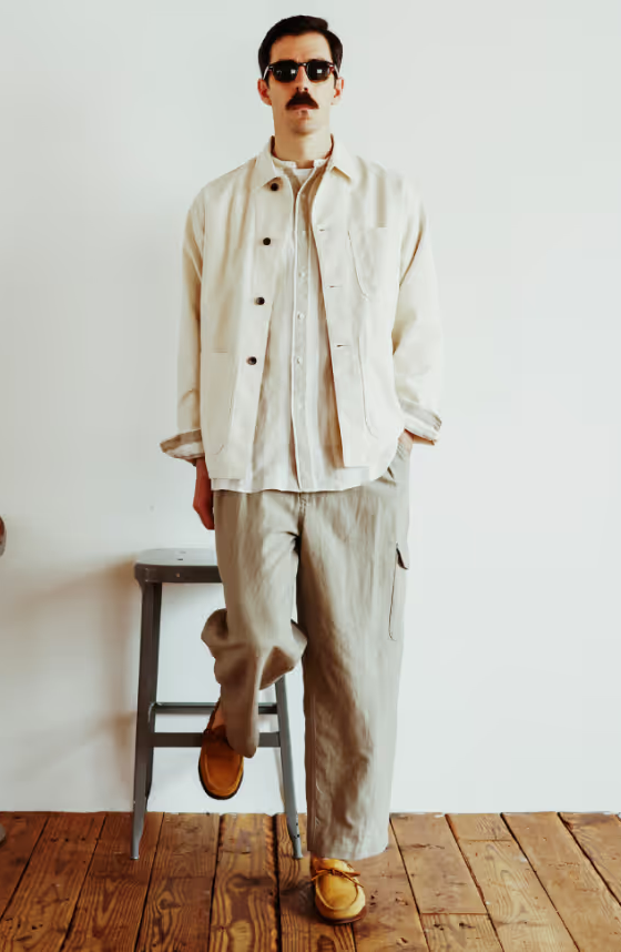 A man in sunglasses wearing a Beams Plus beige overshirt with oversized grey pants and brown shoes