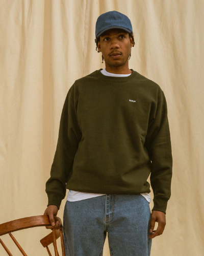 A man wearing a green Adsum sweater, jeans and a blue denim hat