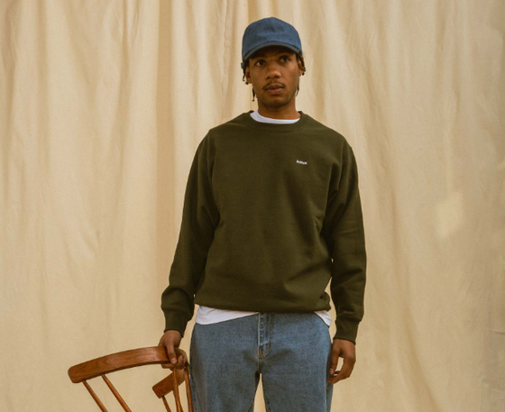 A man wearing a green Adsum sweater, jeans and a blue denim hat