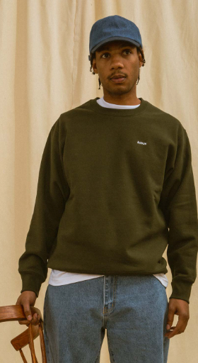 A man wearing a green Adsum sweater, jeans and a blue denim hat