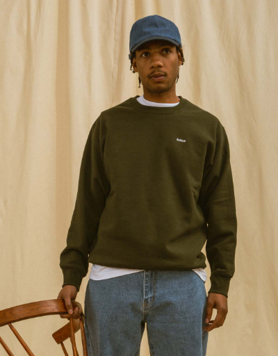 A man wearing a green Adsum sweater, jeans and a blue denim hat