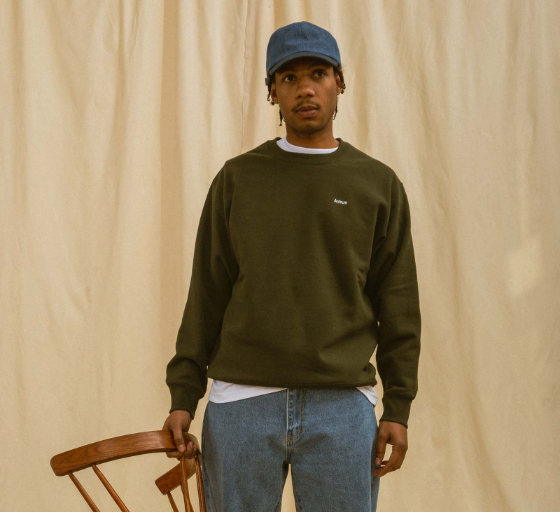 A man wearing a green Adsum sweater, jeans and a blue denim hat